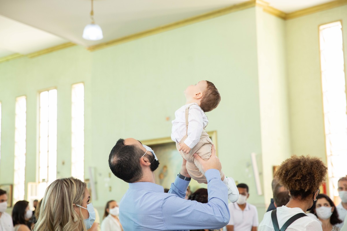 Menino sendo elvantado nos braços do pai no batizado