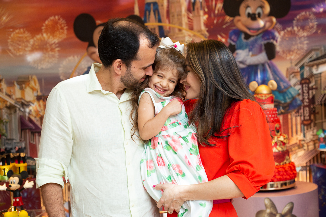 Pai e mãe com a filha menina no colo - festa de aniversário tema da Disney