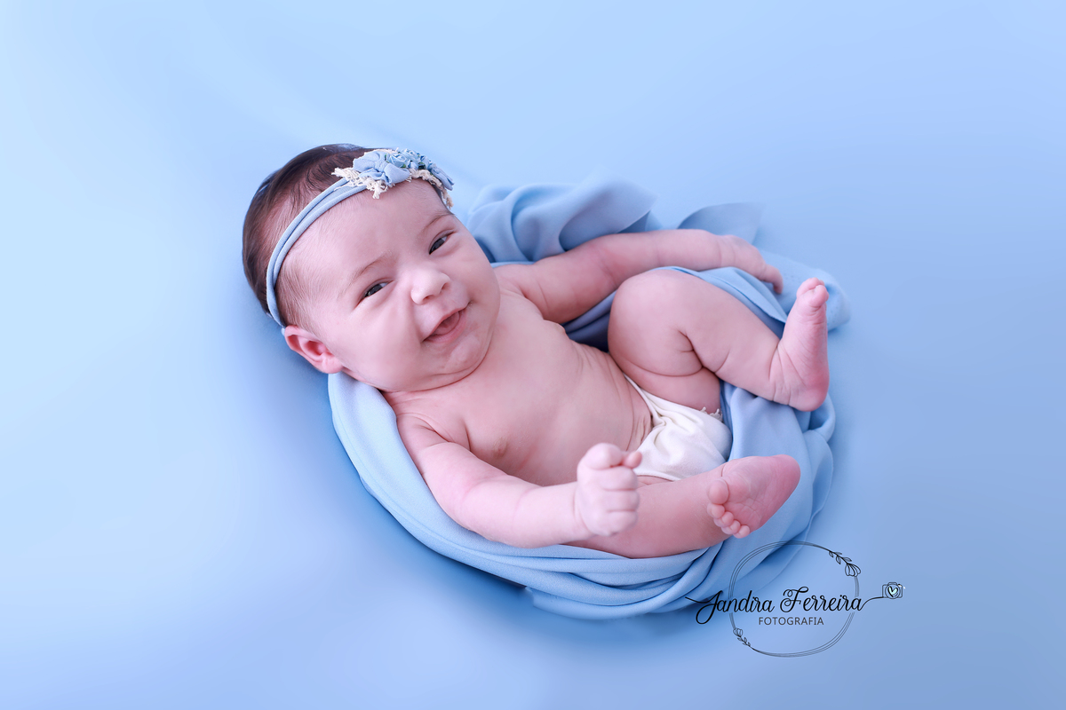 Bebê recém-nascido sorrindo no ensaio newborn.