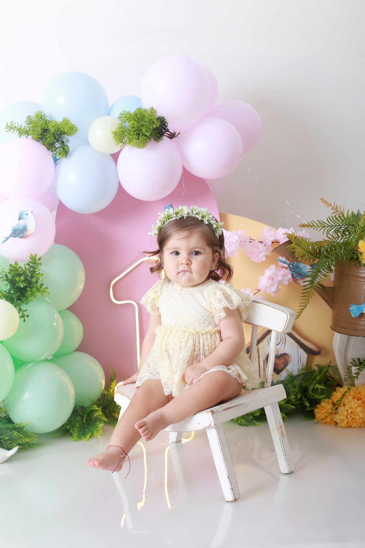 oto do bebê sentado no cenário, enquadrado entre flores, folhas e elementos naturais.