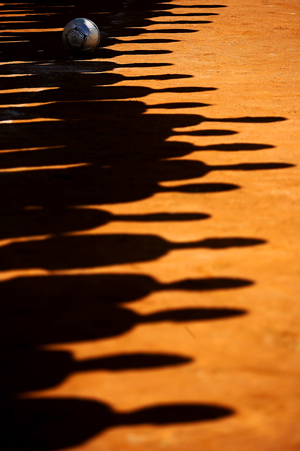 Sombra de crianças no chão de terra durante partida de futebol