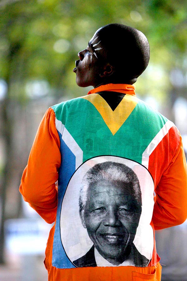 Homem africano usa blusa com foto de Nelson Mandela e rosto pintado enquanto canta