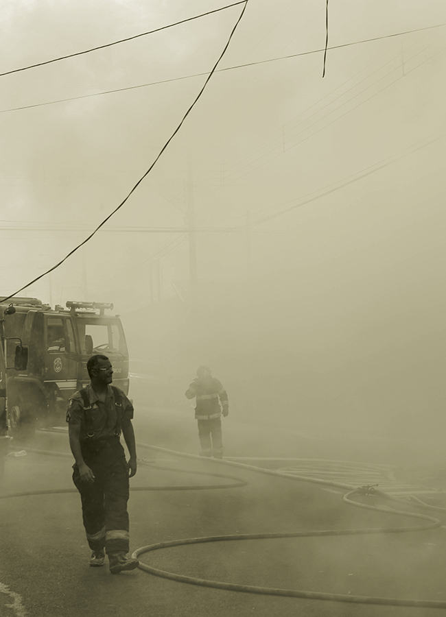 Bombeiros caminham por fumaça após combater incêndio