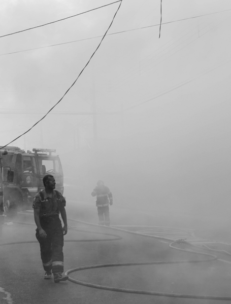 Bombeiros caminham entre a fumaça após apagar incêndio
