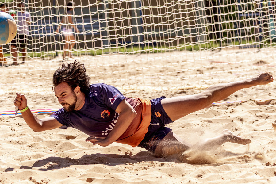 atleta salta na areia durante jogo de vôlei