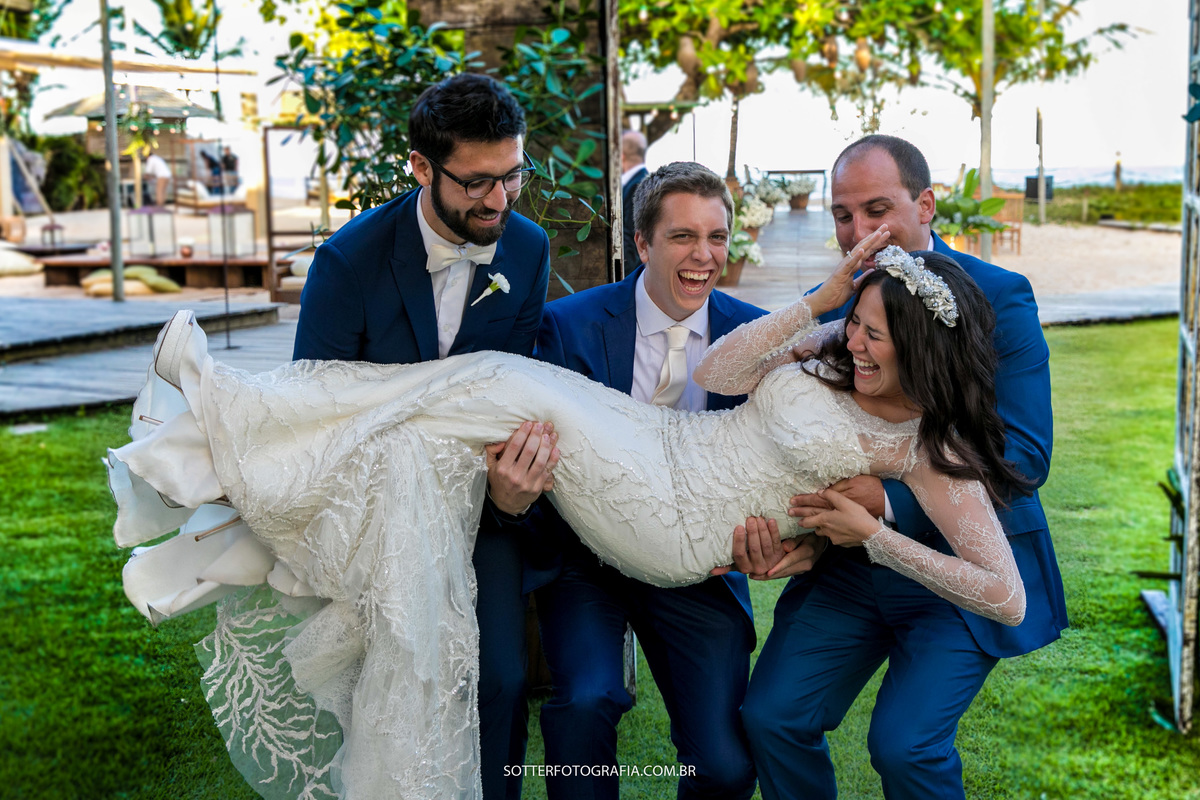 três amigos pegando a noiva no colo e ela sorrindo muito e segurando a coroa com medo de cair