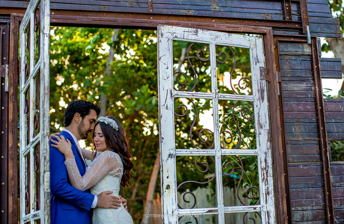 foto linda onde os noivos estão posicionados no portal de madeira e ao fundo uma linda arvore verde 