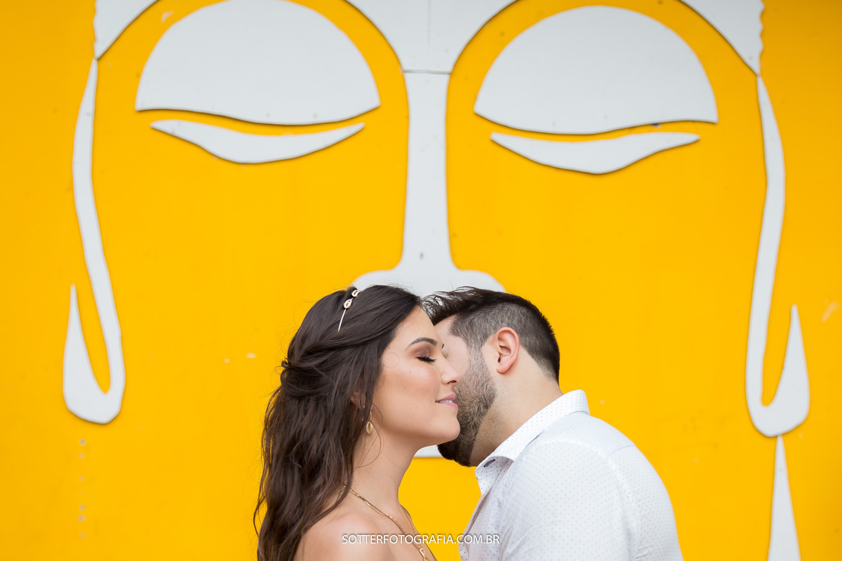 parede amarela com desenho branco dois olhos um nariz e cabelo embaixo o casal se acariciando  sotter fotografia