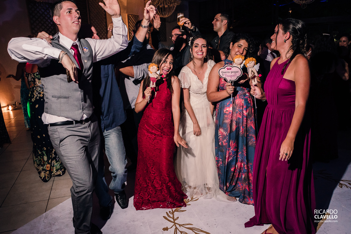 noiva posando com as amigas enquanto o noivo dança- Fotografia de Casamento RJ - Fotografia de Casamento Niterói - Fotógrafo de Casamento RJ - Fotografia de Casamento JF - Fotografo Casamento - Melhores fotos de casamento