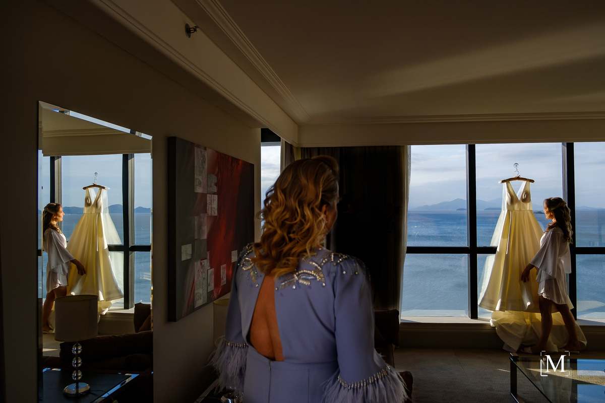 mãe olhando para a noiva com o vestido pendurado