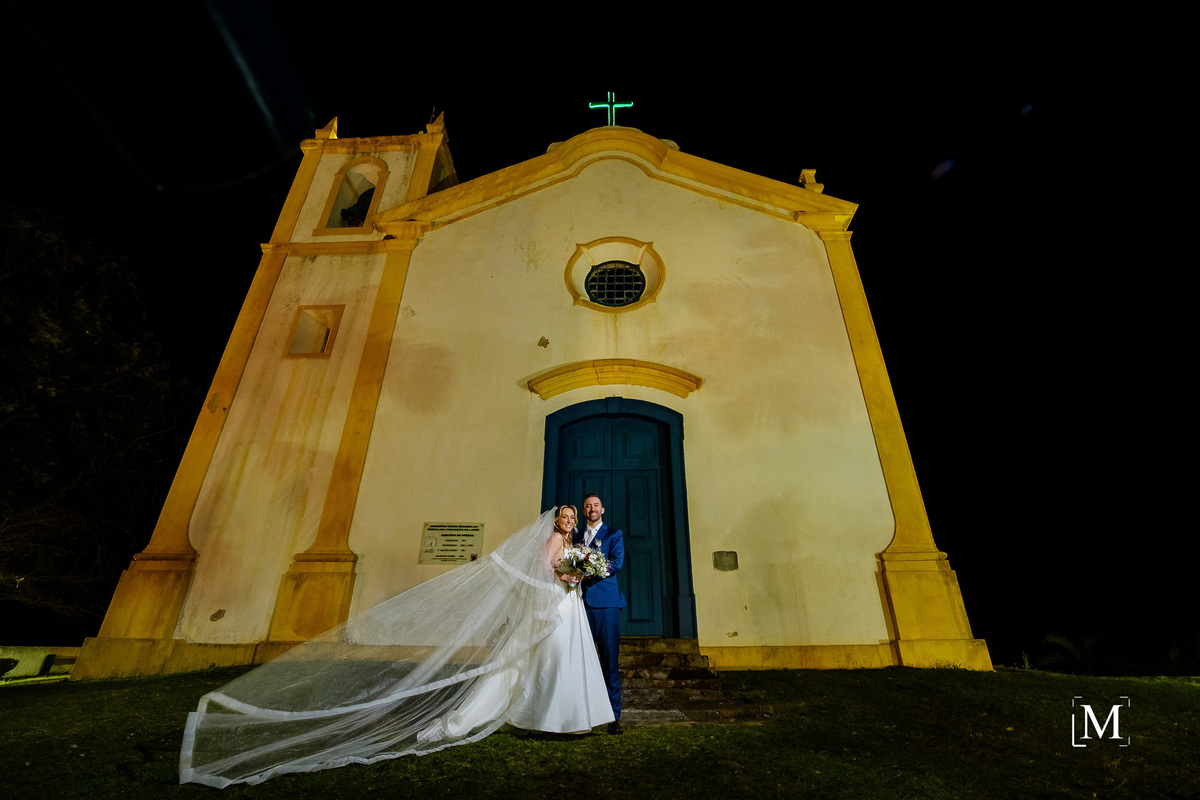 retrato dos noivos em frente a fachada da igreja