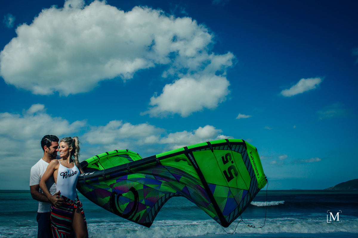 Casal segurando a vela do kitesurf na beira da praia