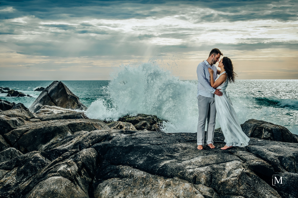 casal nas pedras com onda batendo nas pedras