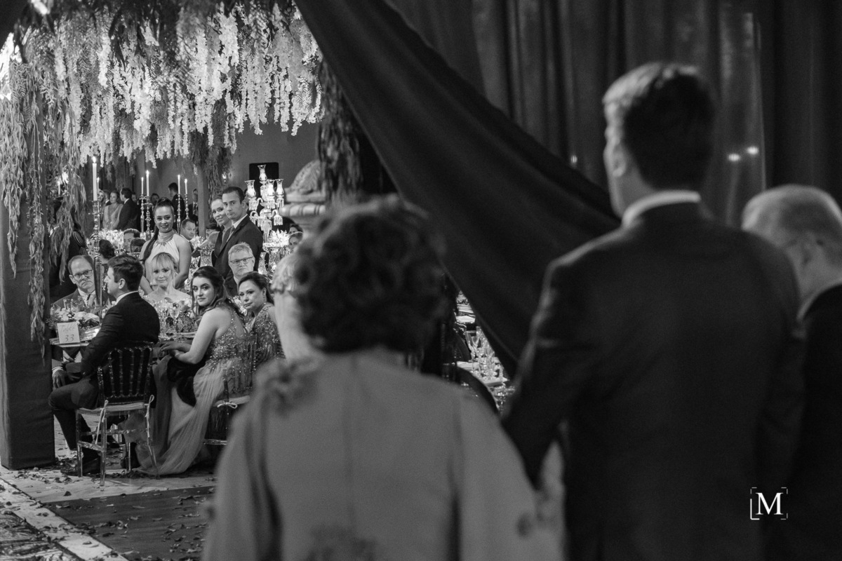 convidados olhando a entrada do noivo com seus pais