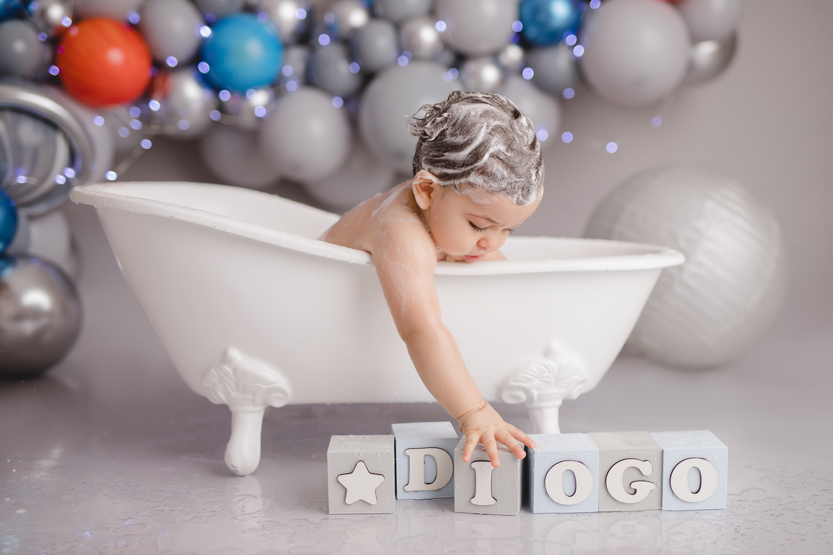 planetas bolo em formato de foguete vermelho e branco em um suporte prata, tomando banho na banheira branca e cubos com letras do nome diogo