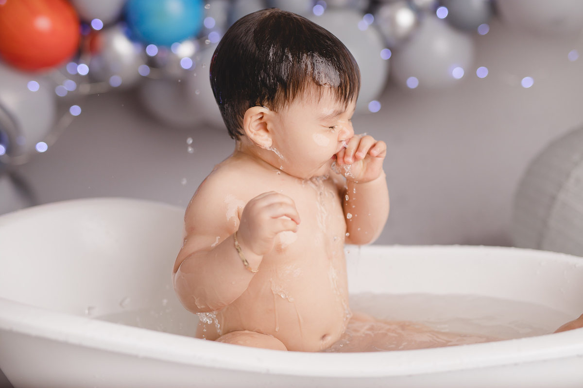 planetas bolo em formato de foguete vermelho e branco em um suporte prata, tomando banho na banheira branca e cubos com letras do nome diogo com as mãos no rosto e água caindo