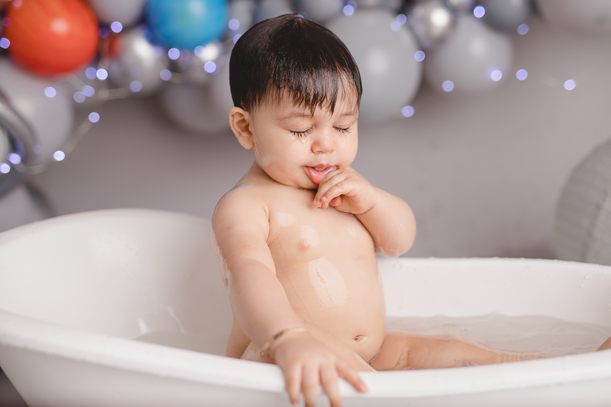 planetas bolo em formato de foguete vermelho e branco em um suporte prata, tomando banho na banheira branca e cubos com letras do nome diogo com as mãos no rosto e água caindo