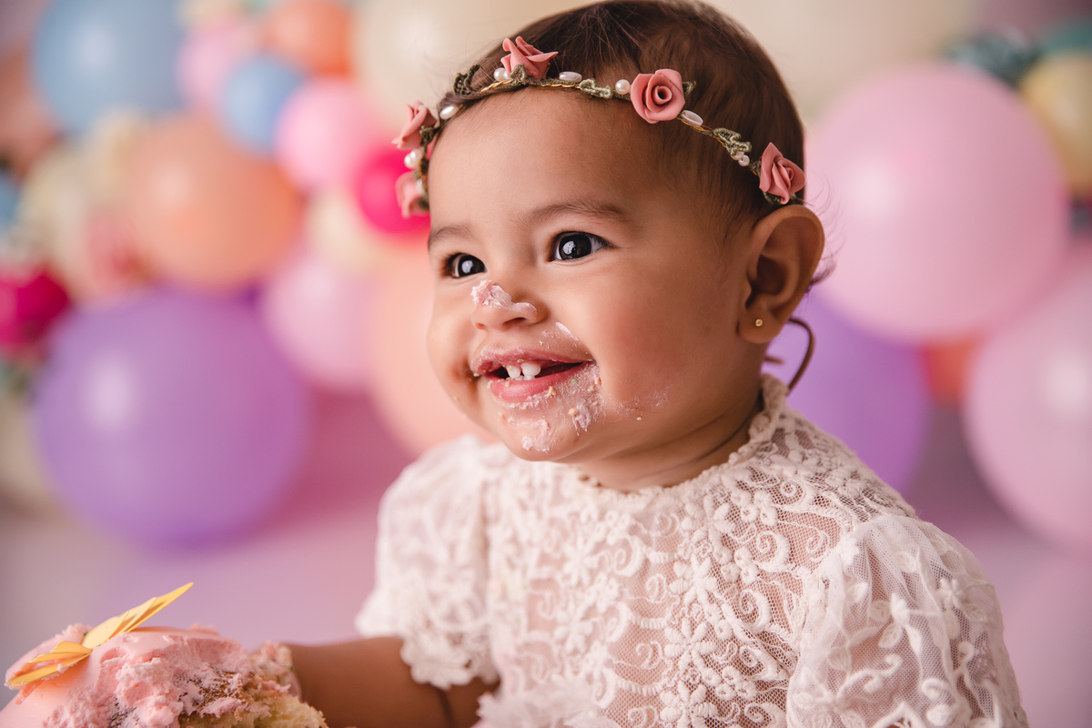 ensaio smash the cake jardim encantado bebe infantil primeiro aninho cadeirinha balões coloridos flores sorrindo roupinha renda e tiara de flores cenário e bolo com borboletas