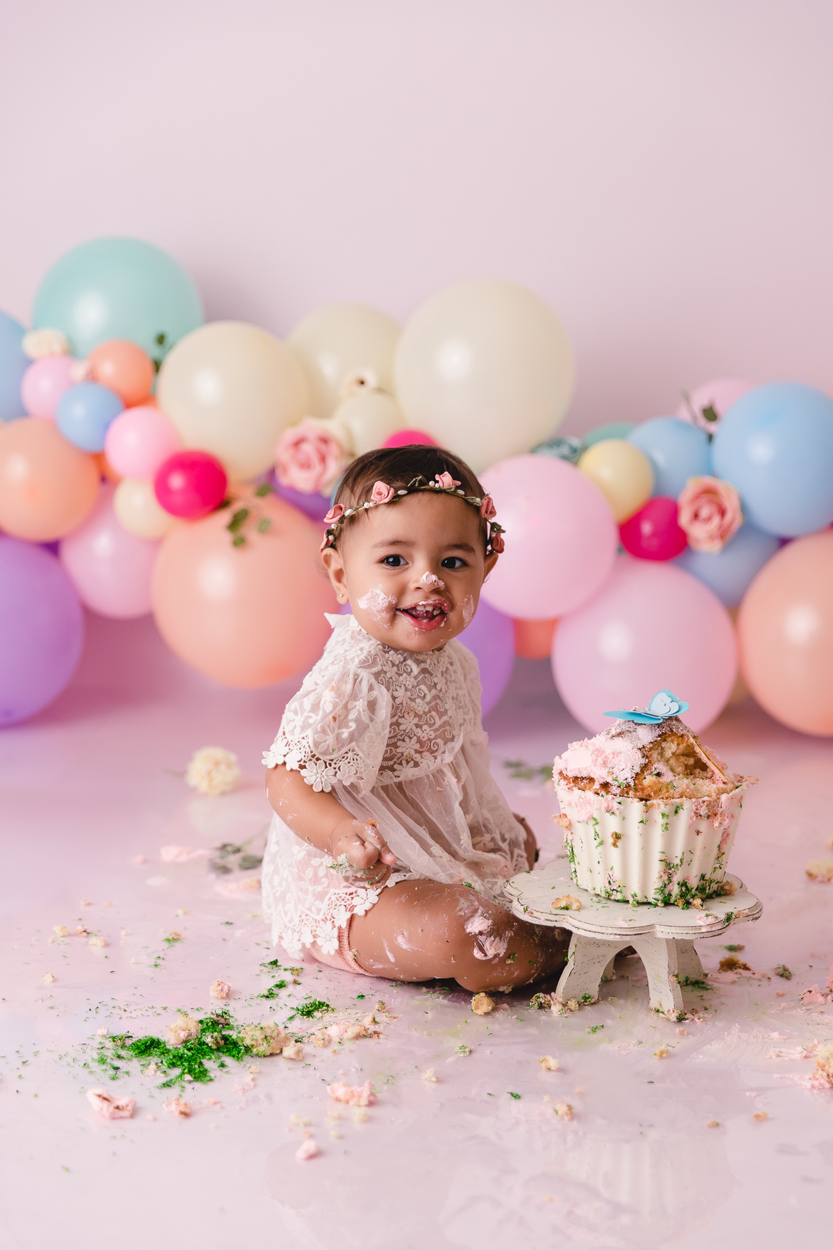 ensaio smash the cake jardim encantado bebe infantil primeiro aninho cadeirinha balões coloridos flores sorrindo roupinha renda e tiara de flores cenário e bolo com borboletas