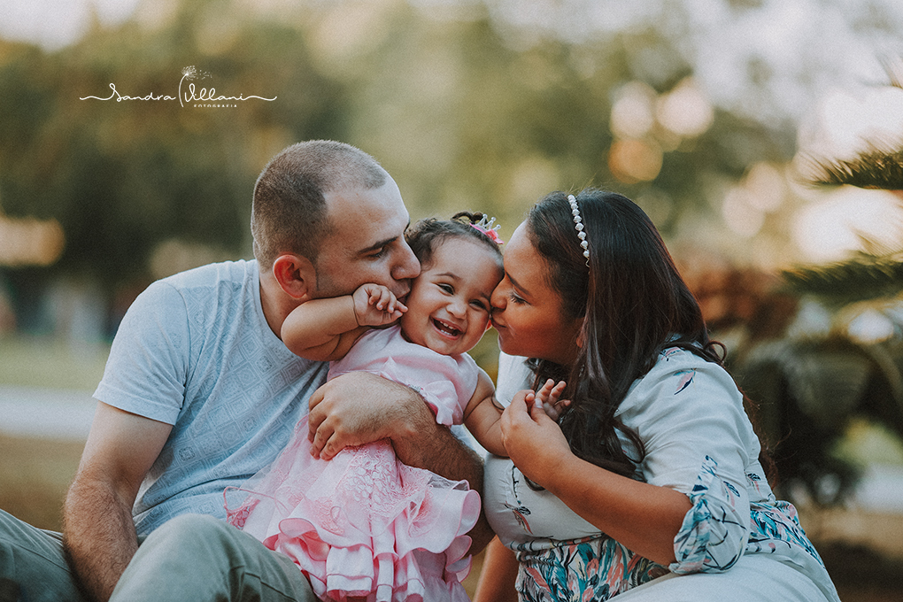 ensaio familia, os pais beijam a filha que sorri alegremente