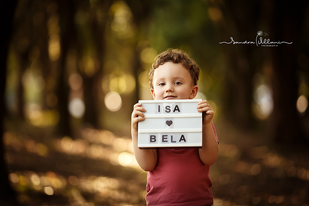 Filho está mostrando uma placa com o nome da irmãzinha Isabela
