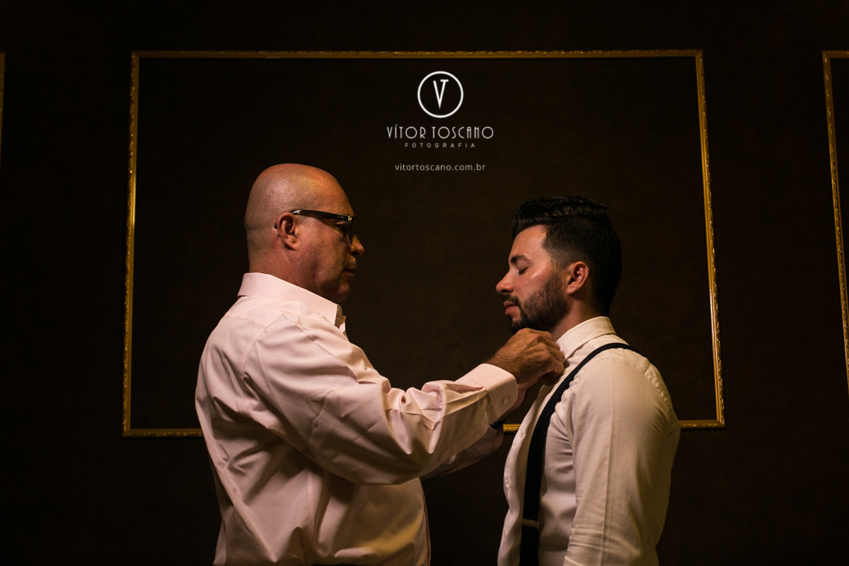 Pai do noivo dando nó na gravata dele no casamento de Karol e Andre, na pousada Macamirim em Natal RN.