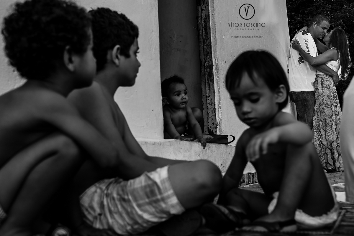 Beijo do casal em meio as crianças durante o ensaio fotográfico de Jucielly e Auderi, em Natal-RN.