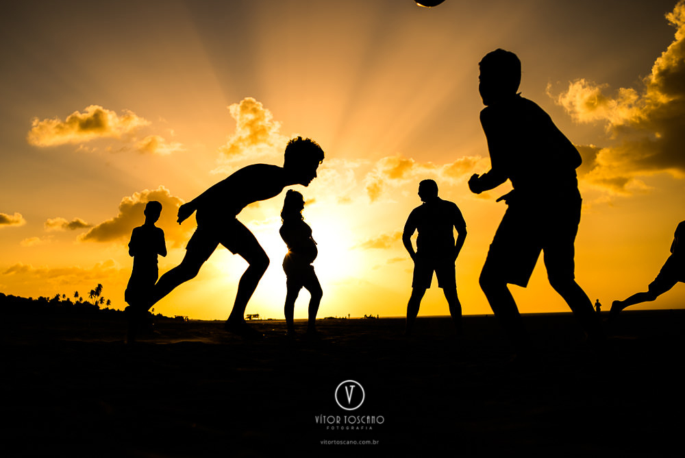 Silhueta do casal em meio as crianças jogando bola, no  ensaio de gestante, em São Miguel do Gostoso-RN.