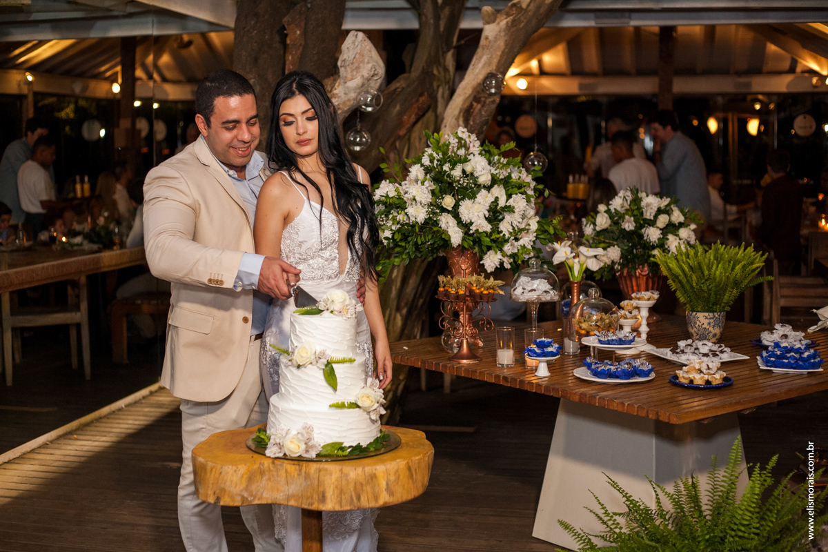 Foto dos noivos cortando o bolo no casamento no restaurante Dona Jô no Porto da Barra em Búzios