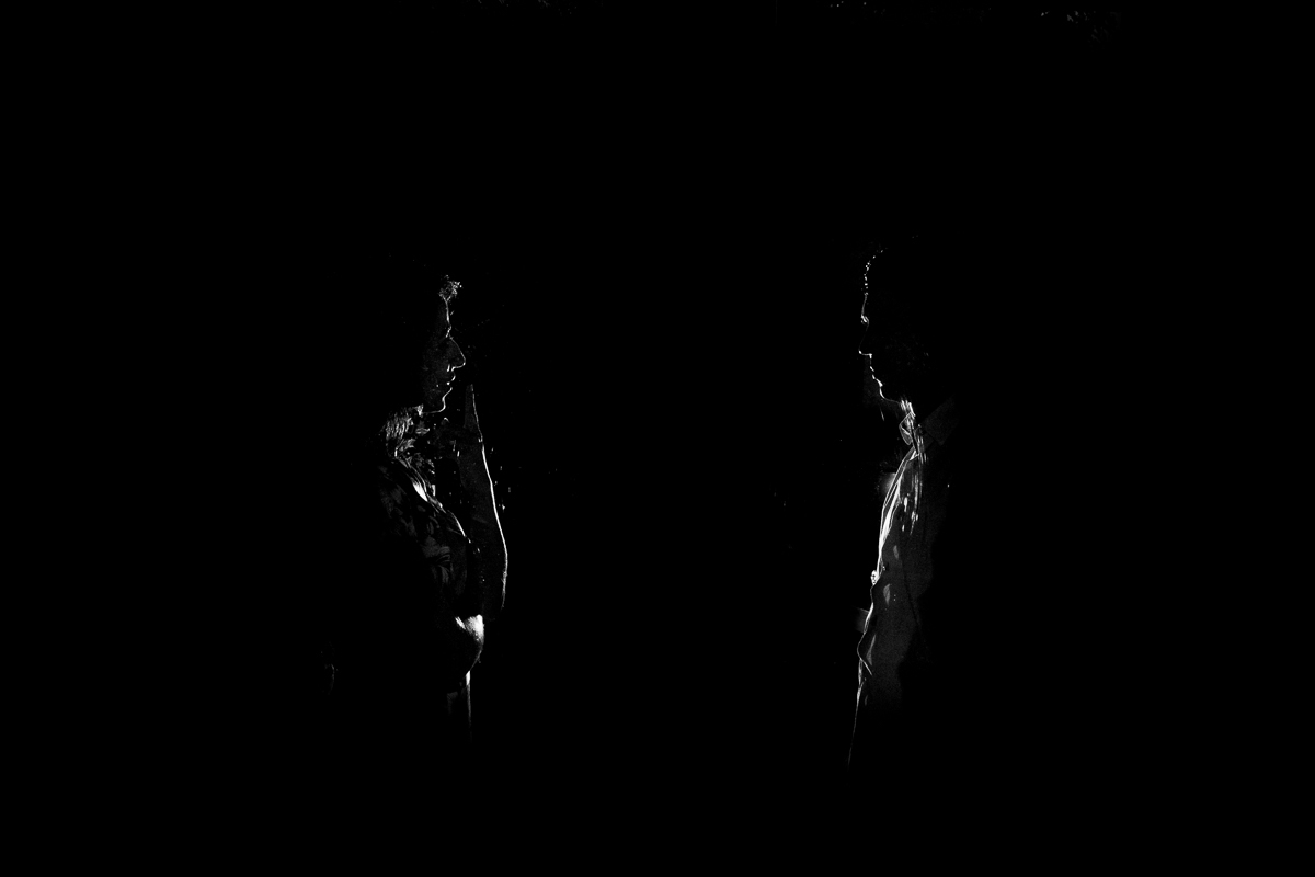 foto preto e branco em contra luz, o casal se olha e sorri enquanto fotografo eles dois através da porta de vidro do quarto onde eles estão hospedados o Guest house ilha splendor