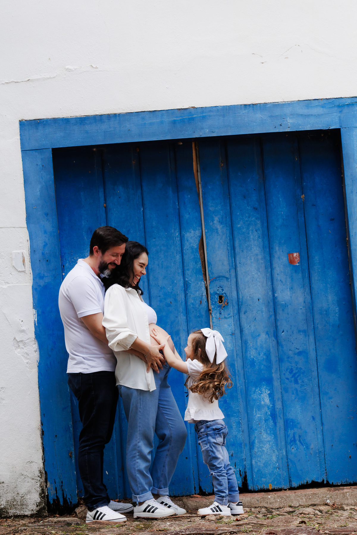Casal e filha celebrando a chegada do bebê durante ensaio gestante em família.