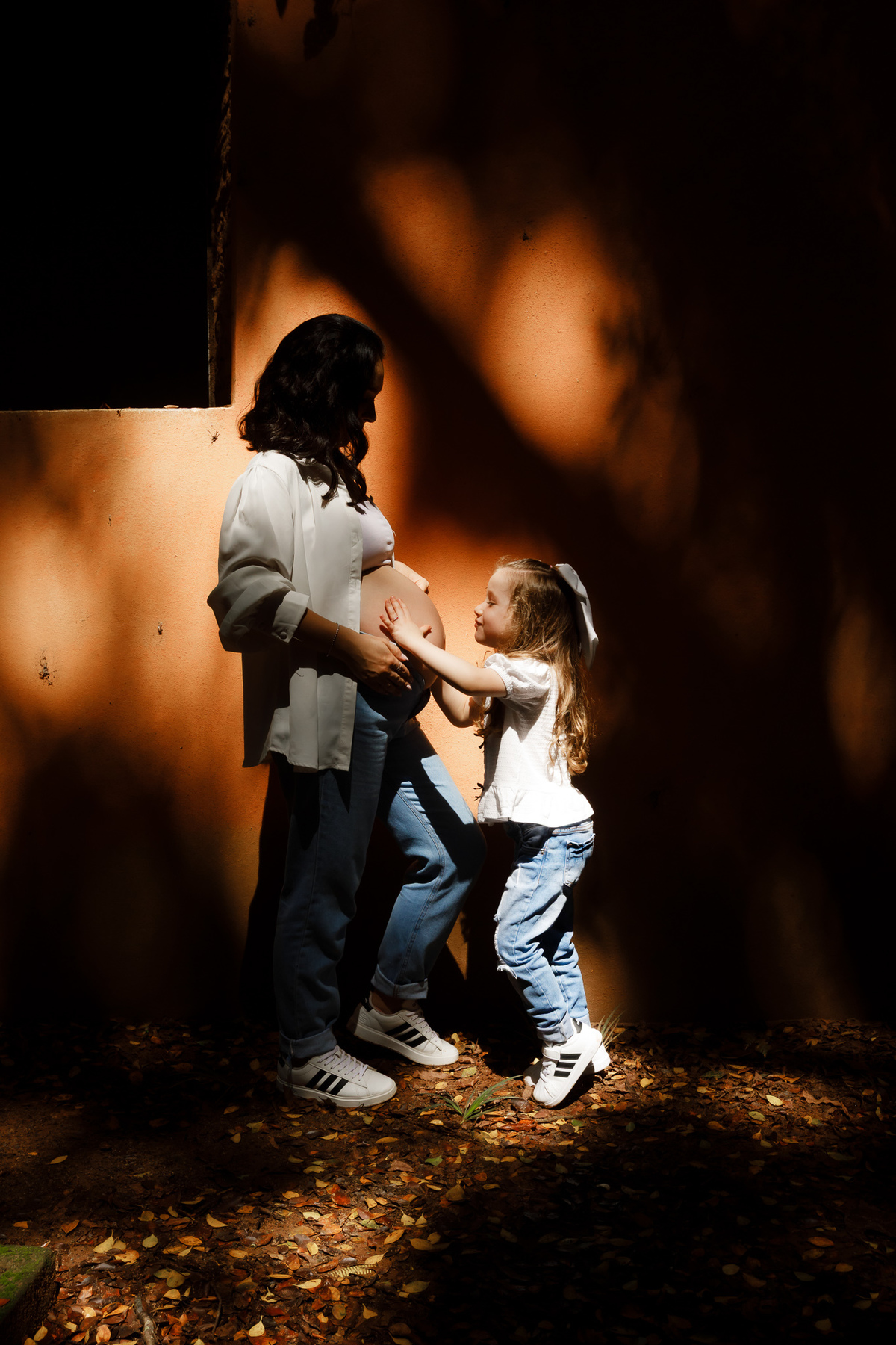 Filha interagindo com a barriga da mamãe durante ensaio gestante em família.