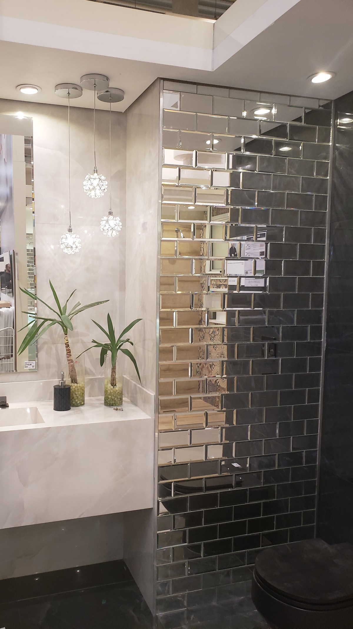 Com um ar mais despojado este ambiente joga revestimento espelhado com revestimento/piso e louças em tom escuro, o encontro do conforto fica por conta dos pendentes de iluminação da iluminação embutida no forro e na delicadeza dos vasos.