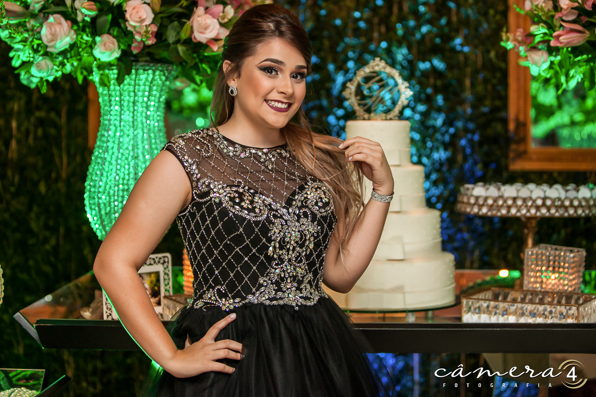 foto da aniversariante durante a festa de 15 anos na frente da mesa do bolo