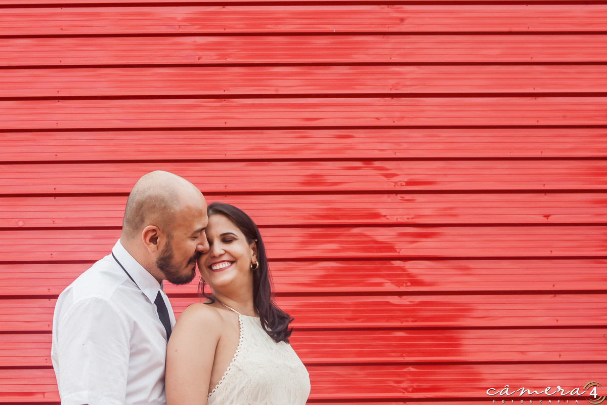 noivos na parede vermelha durante o ensaio pré wedding