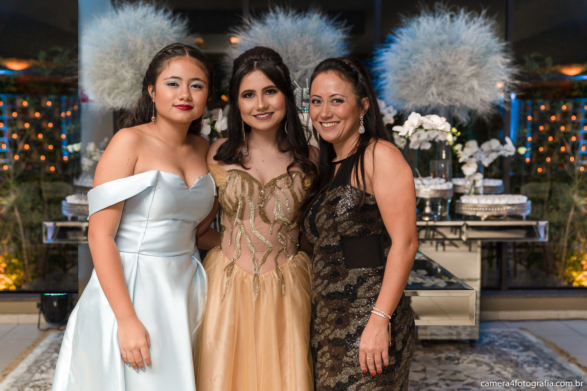 aniversariante com a mãe e a irmã na frente da mesa do bolo