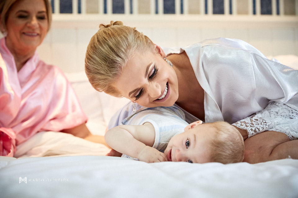 noiva de roupão, sorrindo olhando para bebe deitado na cama no making of