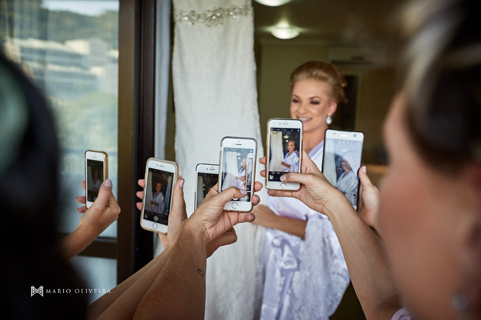 noiva de roupão abraçada no vestido e madrinhas fotografando com seus smartphones no making of
