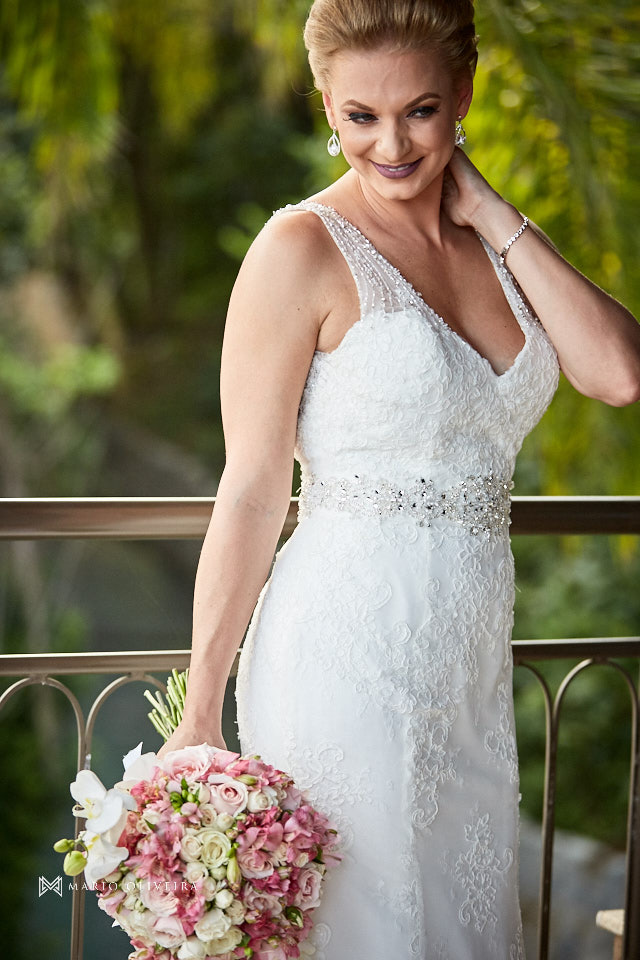 retrato da noiva em pé sorrindo segurando o buque e com a mão no pescoço