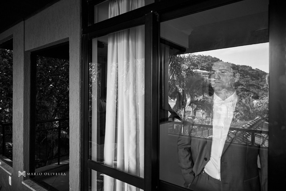 noivo pronto atras da janela da varanda do infinity blue resort balneario camboriu com o reflexo das arvores no vidro