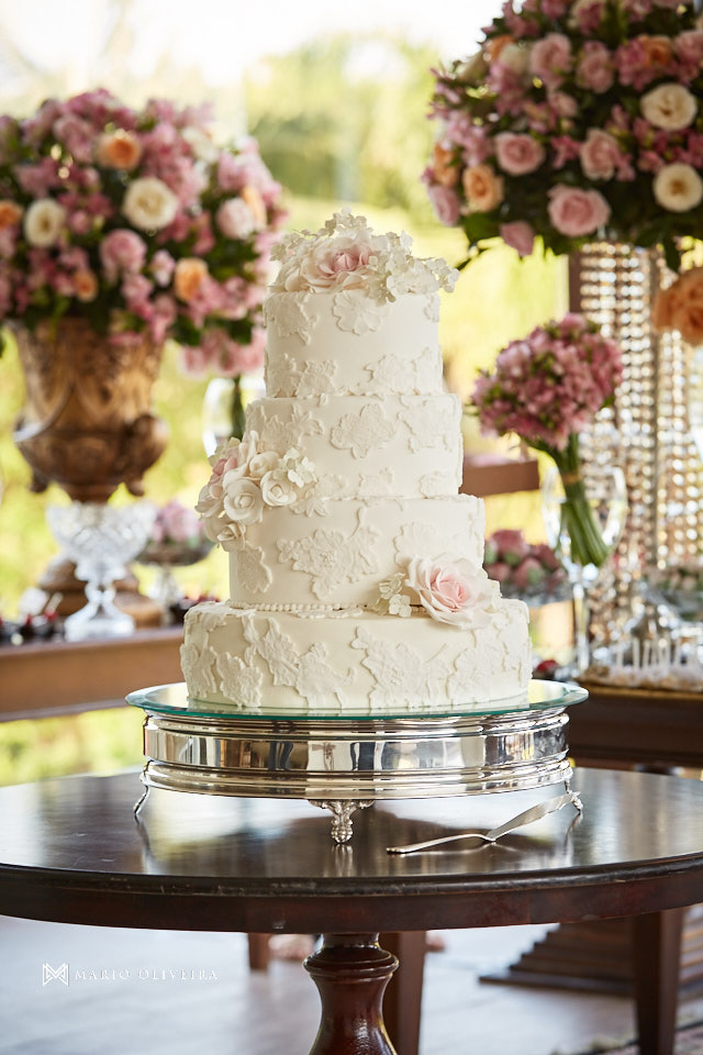 bolo de casamento com quatro andares e mesa de doces ao fundo
