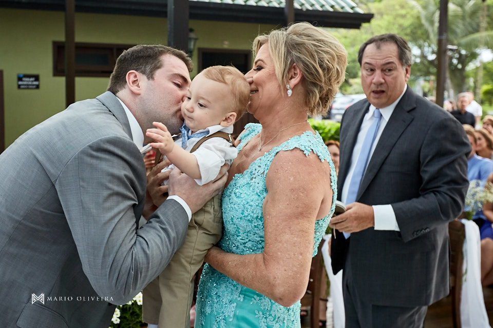 noivo beijando bebe no colo da mão da noiva com seu pai ao fundo