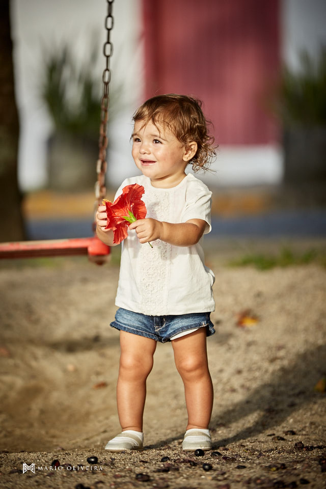 menina brincando no parquinho com uma flor na mão