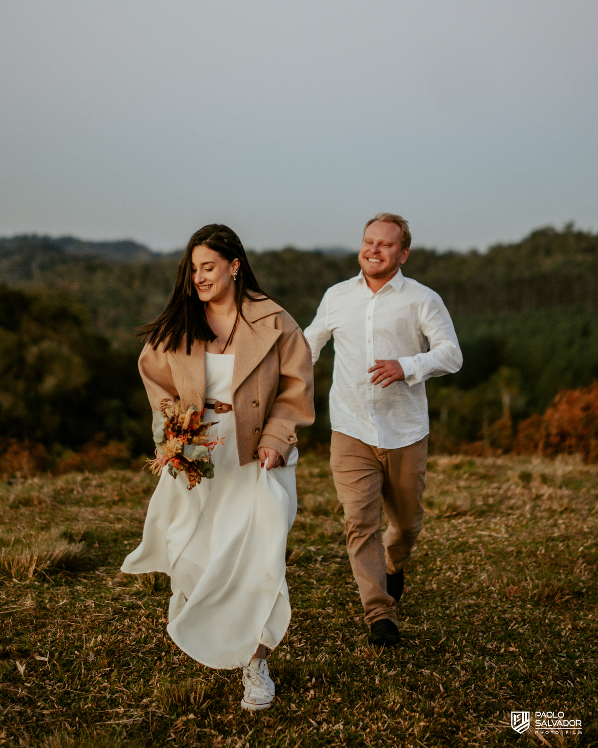 Casal correndo no pôr do sol durante ensaio pré wedding em Benedito Novo SC, fotos espontâneas e emocionantes, fotógrafo de casamento Santa Catarina, ensaio pré casamento criativo