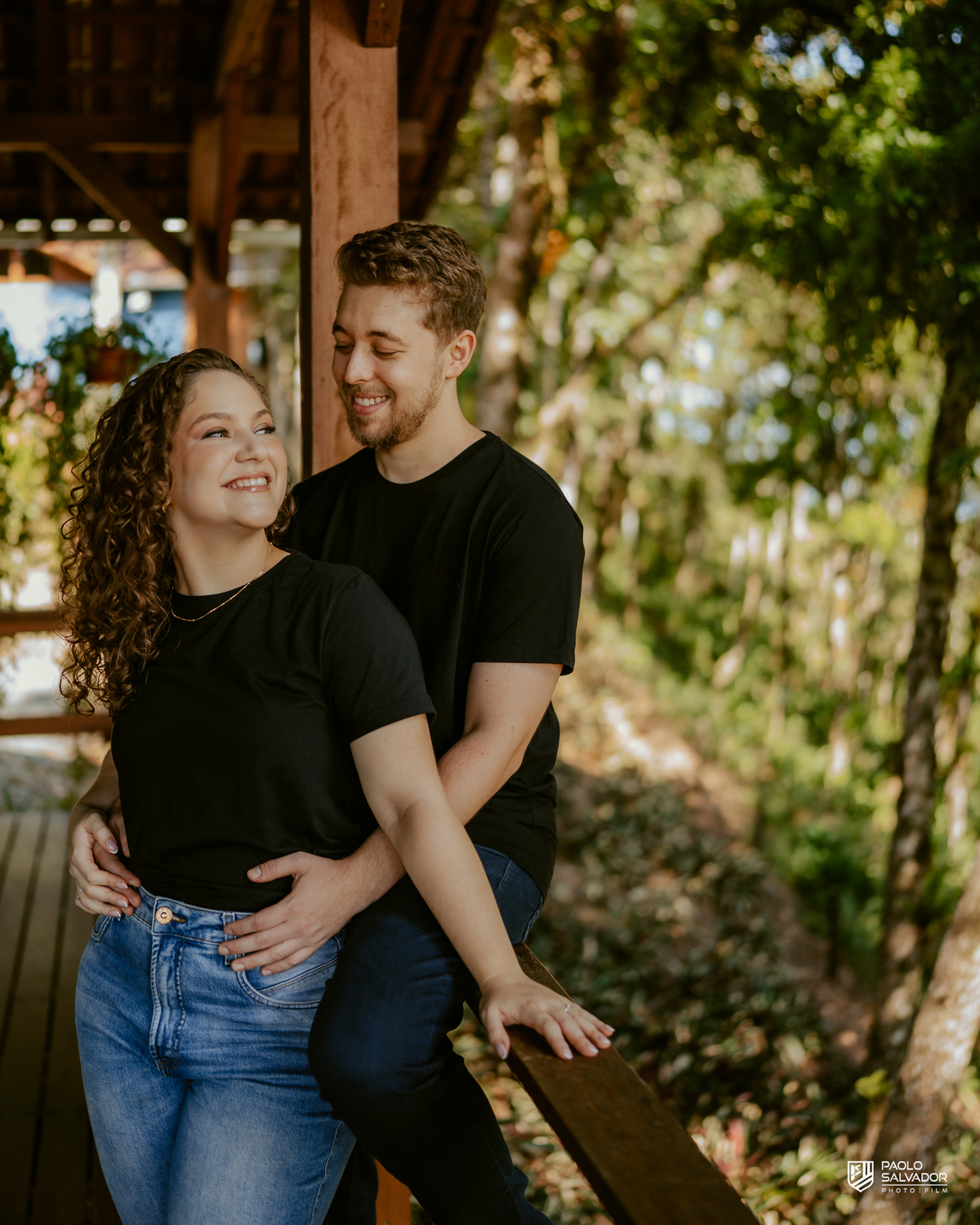 Casal em ensaio pré-wedding em Rio dos Cedros nas Cabanas Morro São Bernardo, abraçados em deck de madeira com natureza ao redor, luz suave e clima romântico, referência para ensaios na Barragem Rio Bonito, Palmeiras e Altos Cedros.