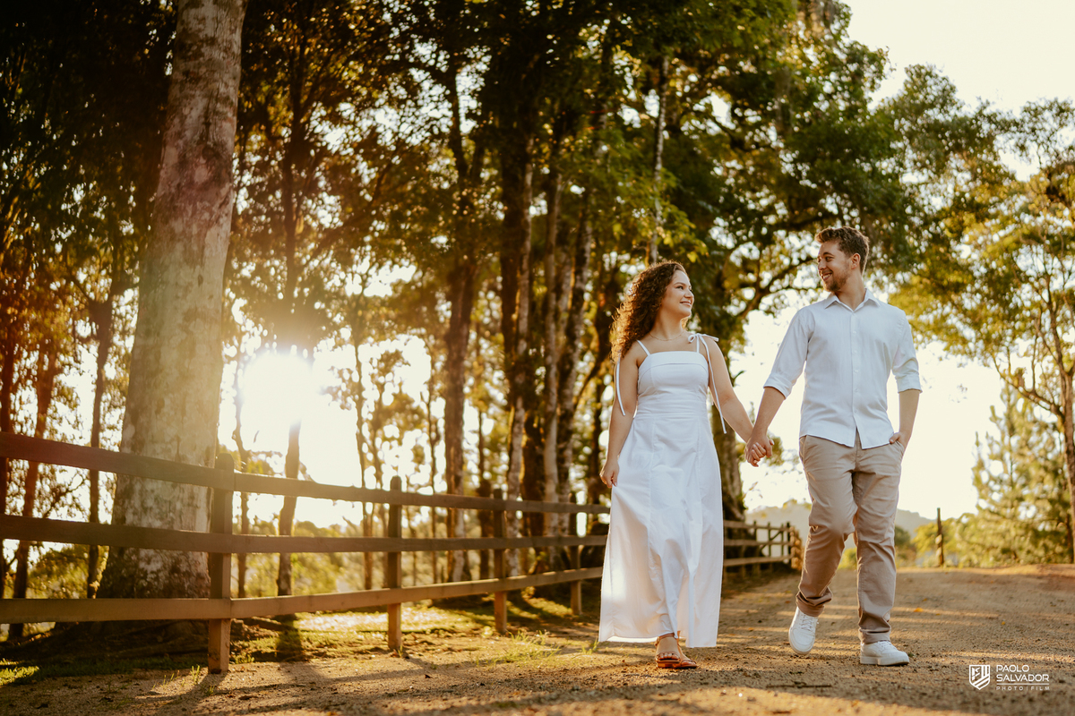 Casal caminhando juntos em estrada rural durante ensaio pré-wedding em Rio dos Cedros, com natureza ao redor e atmosfera leve, inspiração para ensaios em Altos Cedros e região das barragens.