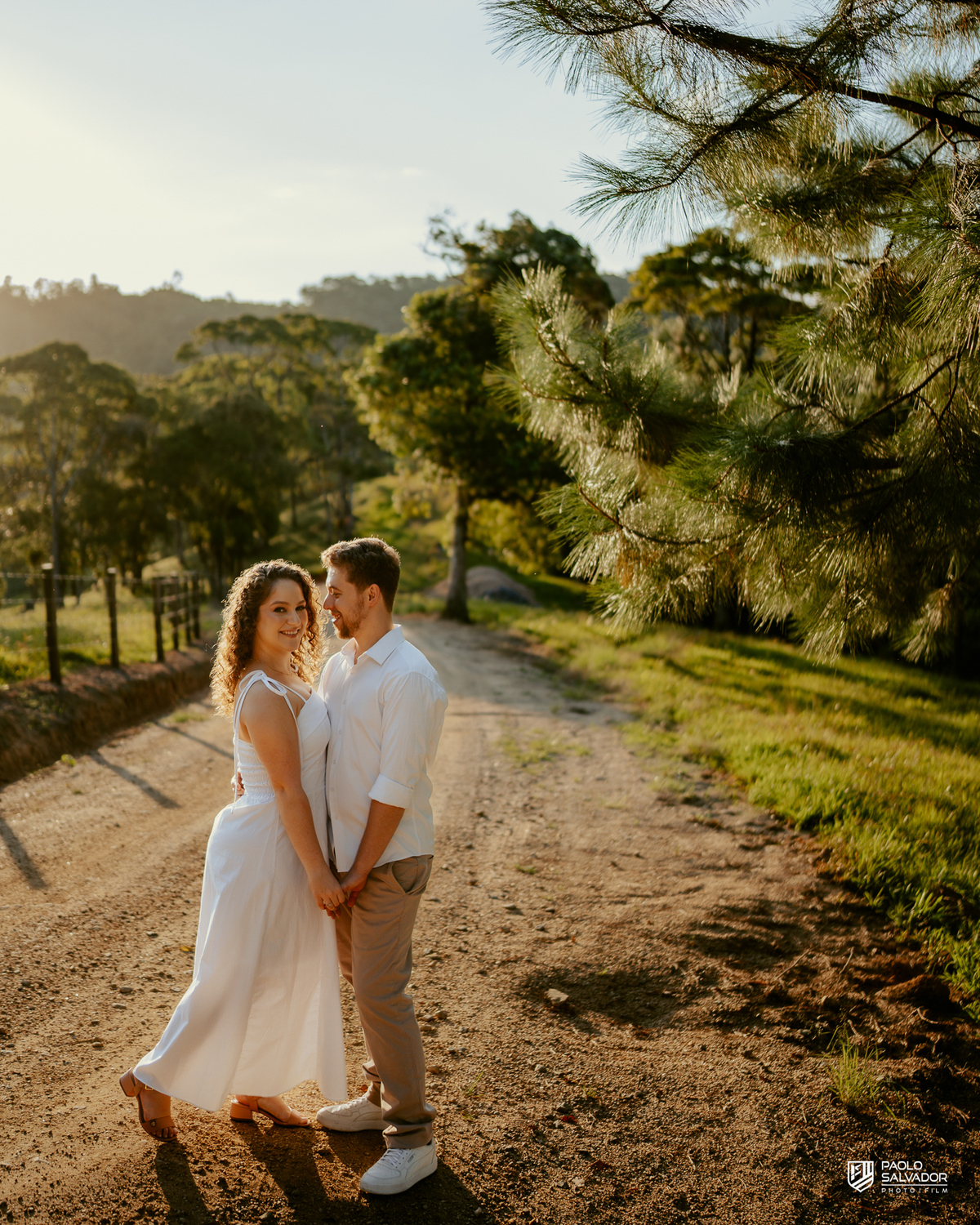Casal caminhando em estrada rural durante ensaio pré-wedding em Rio dos Cedros, com luz dourada e cenário campestre, inspiração para ensaios na Barragem de Palmeiras, Rio Bonito e região.