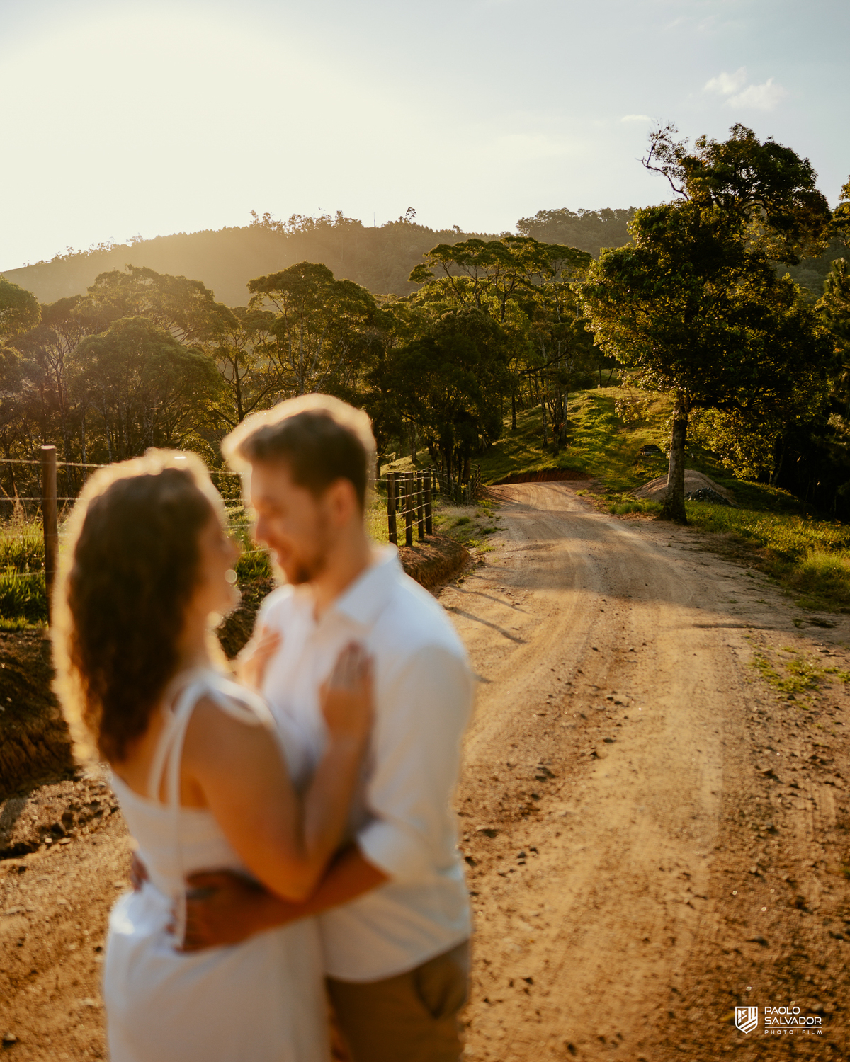 Casal caminhando em estrada rural durante ensaio pré-wedding em Rio dos Cedros, com luz dourada e cenário campestre, inspiração para ensaios na Barragem de Palmeiras, Rio Bonito e região.