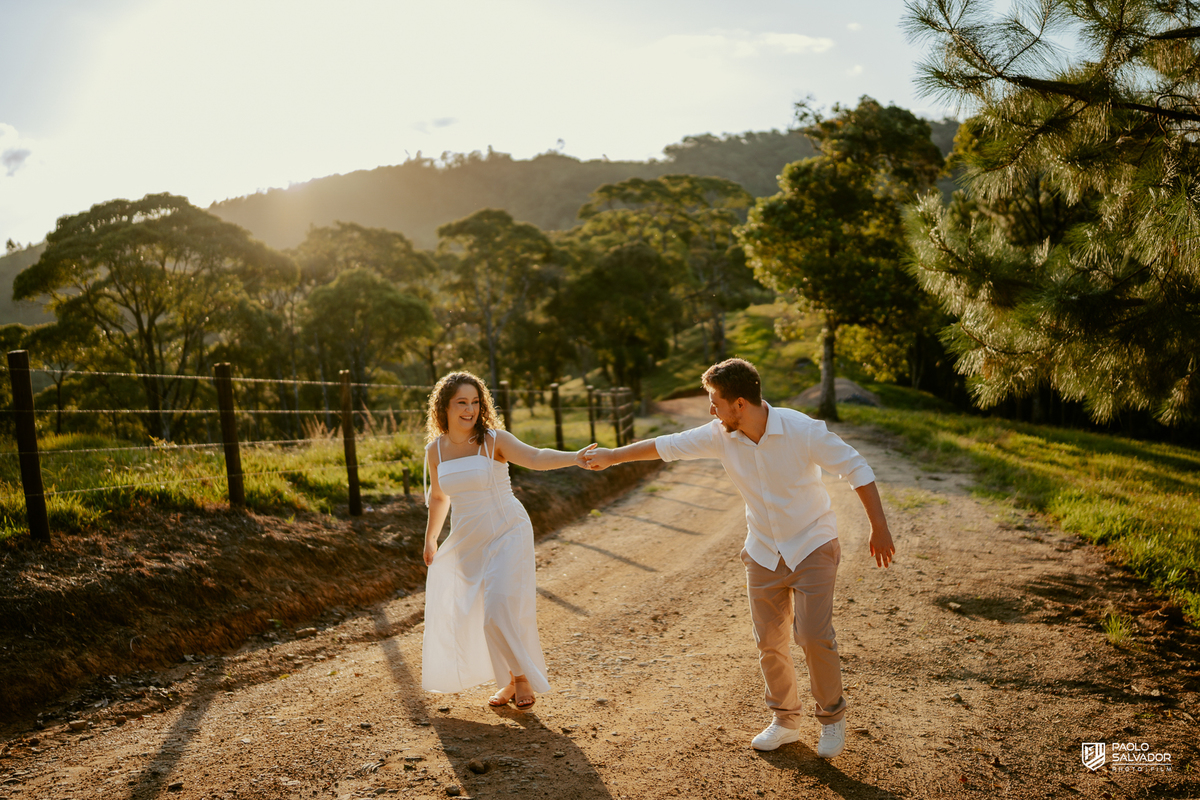 Casal caminhando em estrada rural durante ensaio pré-wedding em Rio dos Cedros, com luz dourada e cenário campestre, inspiração para ensaios na Barragem de Palmeiras, Rio Bonito e região.
