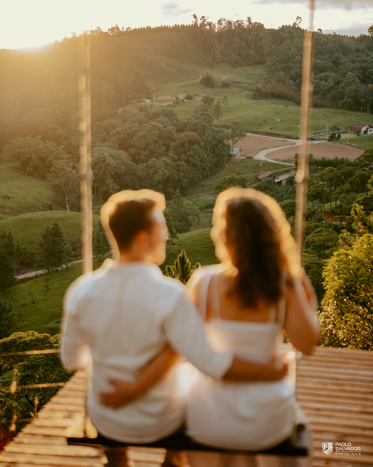 Casal em balanço com vista para montanhas em ensaio pré-wedding em Rio dos Cedros, pôr do sol dourado e paisagem natural, referência para ensaios na Barragem Rio Bonito, Palmeiras e Região dos Lagos.